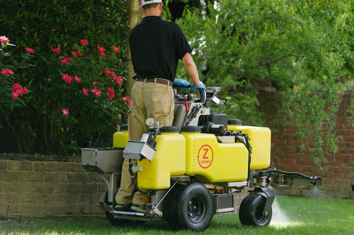 lawn care technician fertilizes lawn with ride on liquid spray machine